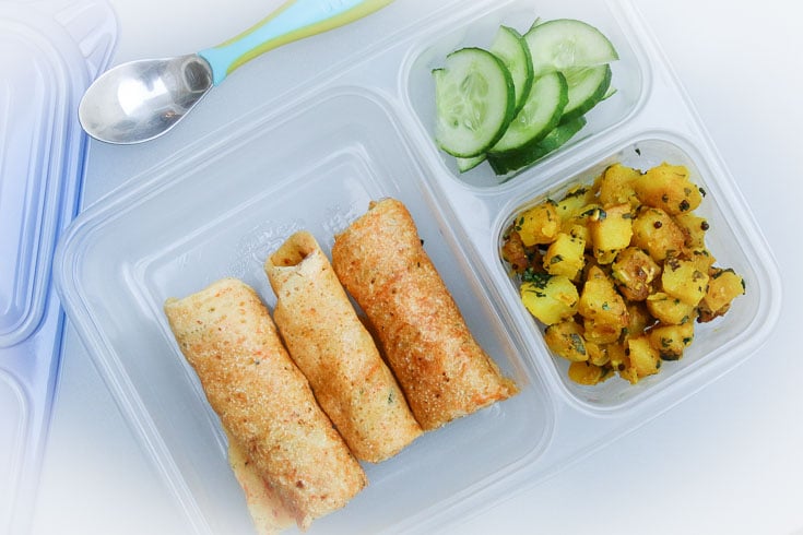 Overhead photograph of easy school lunch idea consisting of dosa, curried potatoes, and cucumbers. 